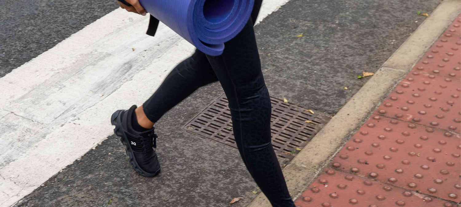Woman walking across the road with yoga mat and knee padded leggings 