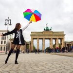 A woman standing in front of a historic monument in Berlin holding a colorful umbrella to the sky